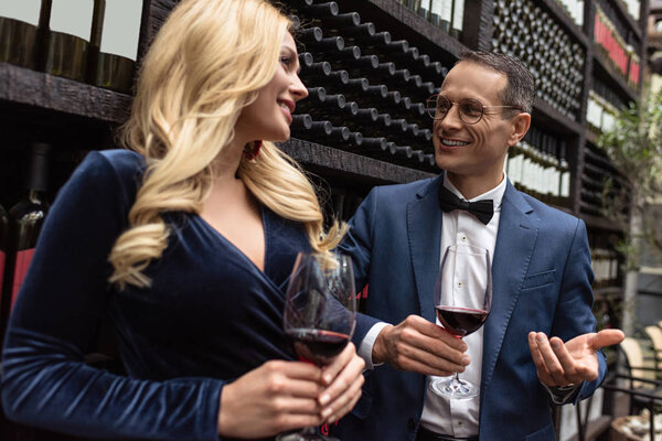 attractive adult couple drinking wine in front of wine storage shelves