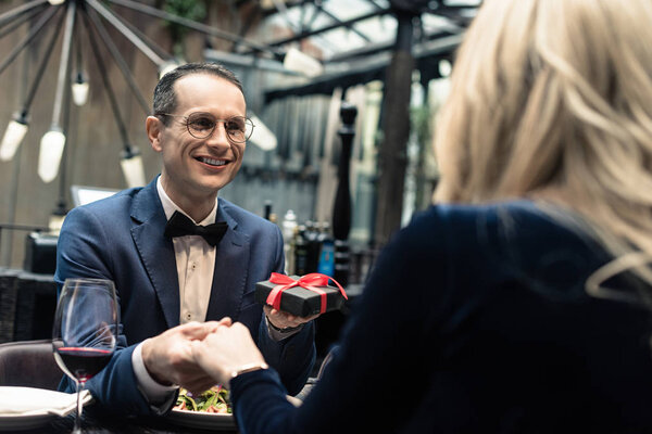 handsome happy man presenting valentines day gift to girlfriend at restaurant