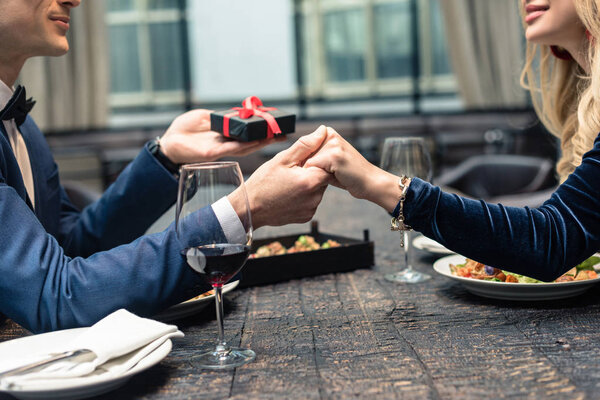 cropped shot of of man presenting valentines day gift to girlfriend at restaurant