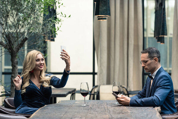 side view of unhappy adult couple using smartphones at restaurant