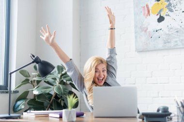 happy businesswoman screaming with hands up and looking at laptop clipart