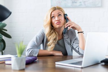 irritated businesswoman talking by telephone in office clipart