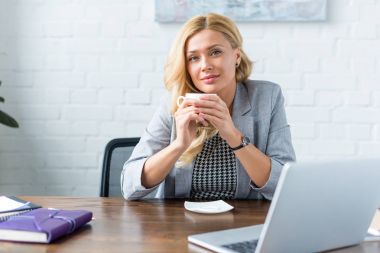 kahve ofiste tutarak ve kameraya bakarak neşeli işkadını