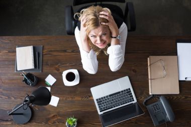 overhead view of stressed businesswoman touching head with hands and looking at camera in office clipart