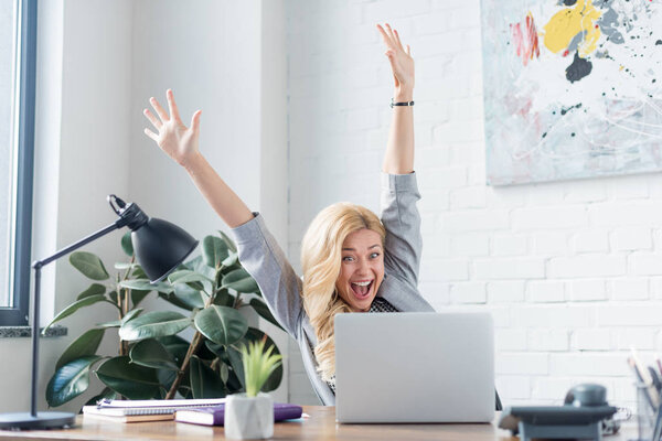 happy businesswoman screaming with hands up and looking at laptop