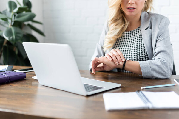 cropped image of businesswoman looking at watch on office with laptop