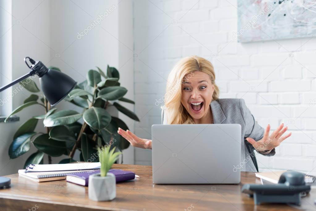 surprised businesswoman looking at laptop in office