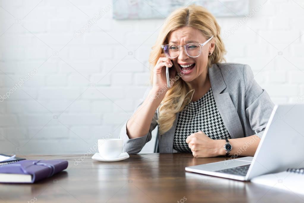 shocked screaming businesswoman talking by smartphone in office