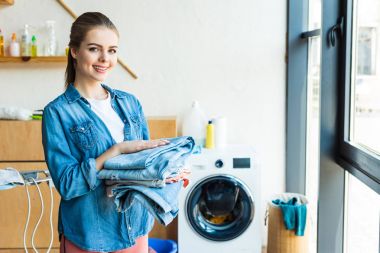 Giysi tutarak ve kamera çamaşır makinesi evde yakın dururken gülümseyen genç kadın