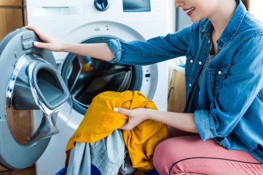 cropped shot of smiling young woman taking laundry from washing machine