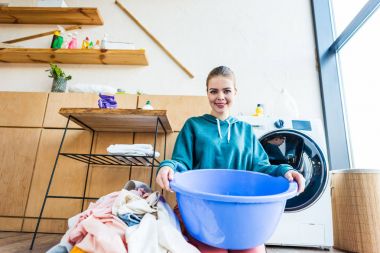 plastik Havzası tutarak ve elbise ve çamaşır makinesi diz çökmüş iken kameraya gülümseyen genç kadın