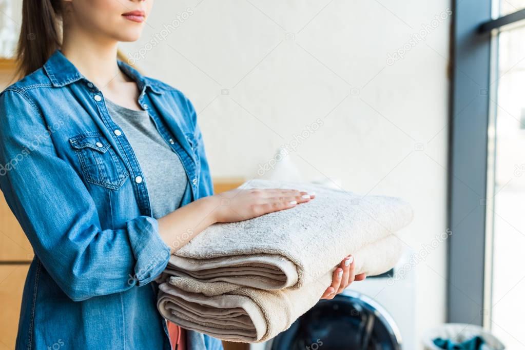 cropped shot of young woman holding clean towels at home