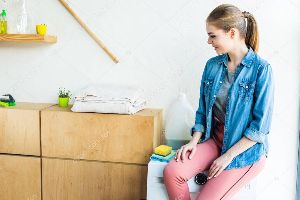 Smiling Young Woman Sitting On Washing Machine And Looking Away At Home 184076174 Larastock