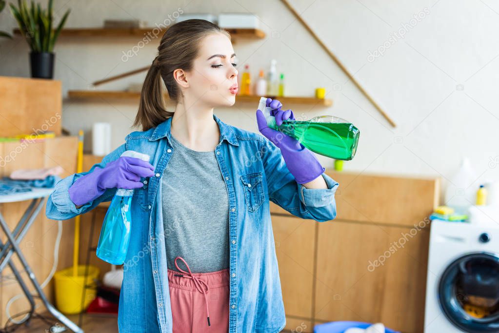 beautiful young woman in rubber gloves holding plastic bottles with cleaning fluids