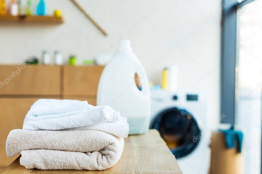 close-up view of stacked clean towels and plastic container with cleaning fluid on wooden table at home 