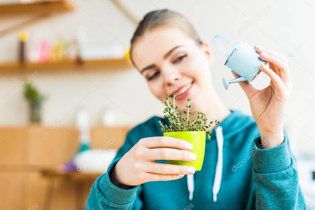 happy young woman watering potted plant at home