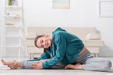 Yoga mat germe ve evde kameraya bakarak gülümseyen kız