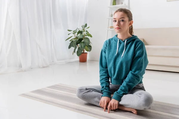 Mädchen Sitzt Lotusposition Auf Yogamatte Und Schaut Hause Die Kamera — Stockfoto