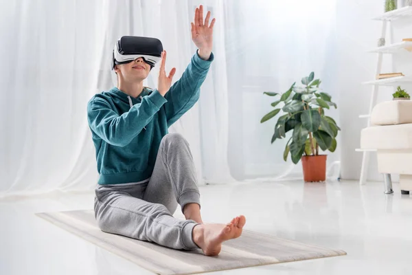 Mädchen Sitzt Auf Yogamatte Mit Virtual Reality Headset Und Berührt — kostenloses Stockfoto
