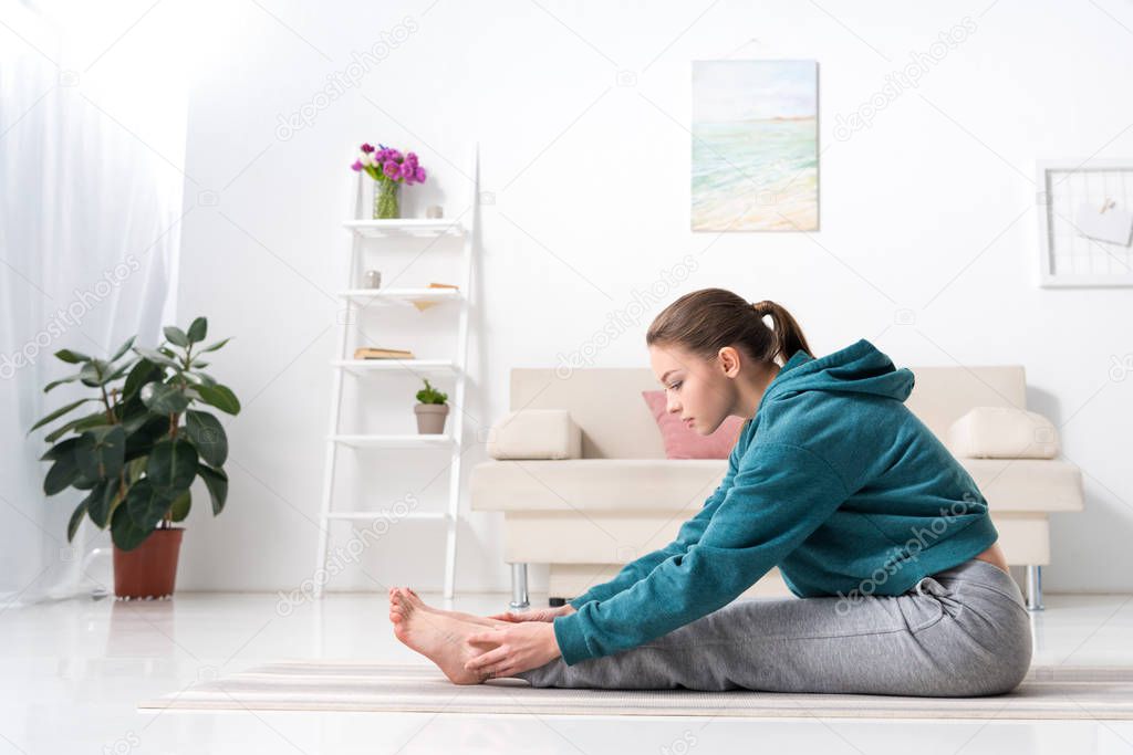 side view of girl exercising on yoga mat at home