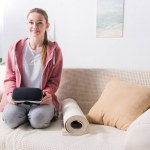 Chica sonriente sosteniendo auriculares de realidad virtual y mirando a la cámara en casa