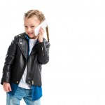 Smiling stylish kid wearing leather jacket and talking on smartphone isolated on white