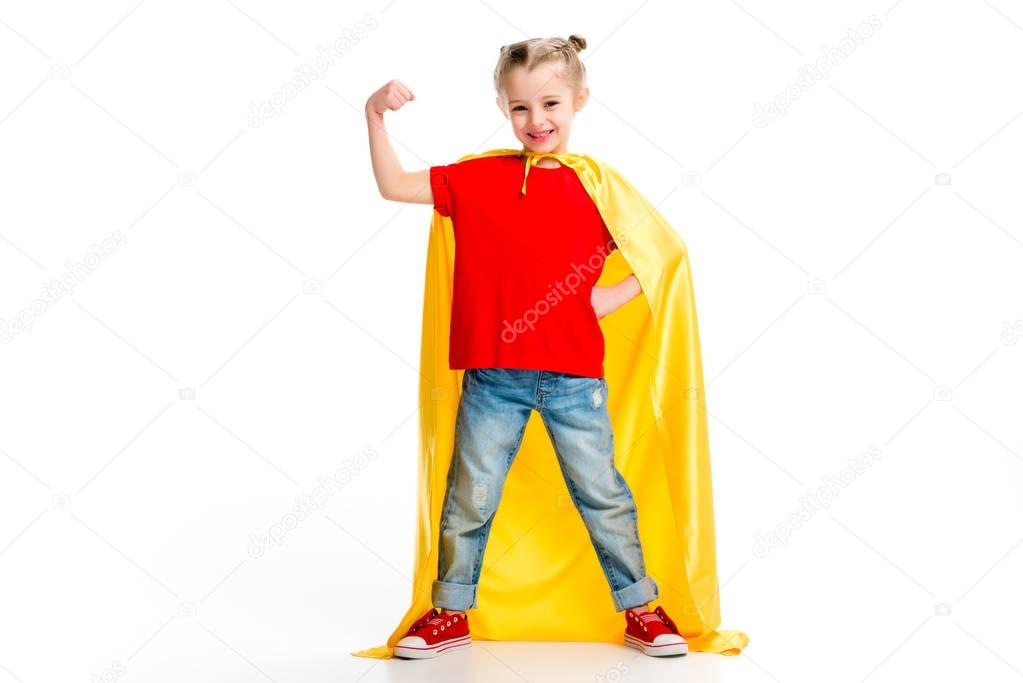 Smiling supergirl in yellow cape showing muscles on hand isolated on white