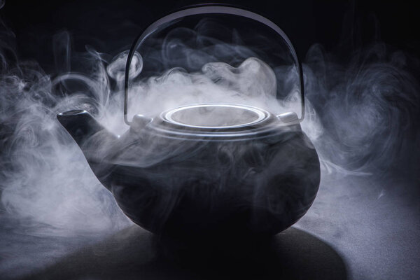 close-up view of black kettle with hot steam on black 