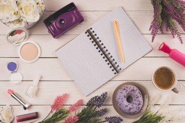 top view of empty open notebook with pen, camera, flowers, cosmetics and cup of coffee with doughnut on table top clipart