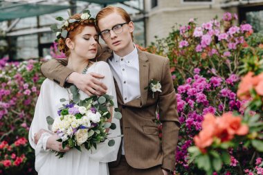 şık genç damat ve gelin birlikte Botanik bahçesinde duran düğün buketi ile 
