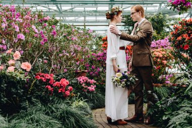 güzel şık genç Düğün çifti birbirine Botanik bahçesinde çiçekler arasında dururken bakarak yan görünüm
