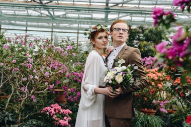 buket tutarak ve uzak birlikte Botanik bahçesinde çiçekler arasında ayakta iken arıyorum güzel zarif genç Düğün çifti