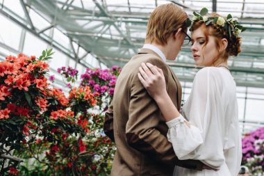 Botanik bahçesinde çiçekler arasında kucaklayan güzel genç zarif Düğün çifti 