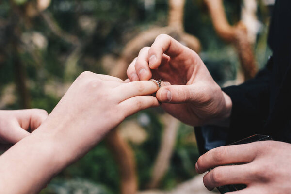 cropped shot of man putting wedding ring on finger of young bride