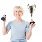 Senior sportswoman with trophy and dumbbell isolated on white