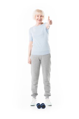 Senior sportswoman showing thumb up gesture and dumbbells on floor isolated on white clipart