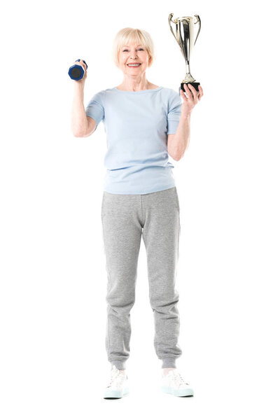 Smiling senior sportswoman with trophy and dumbbell isolated on white