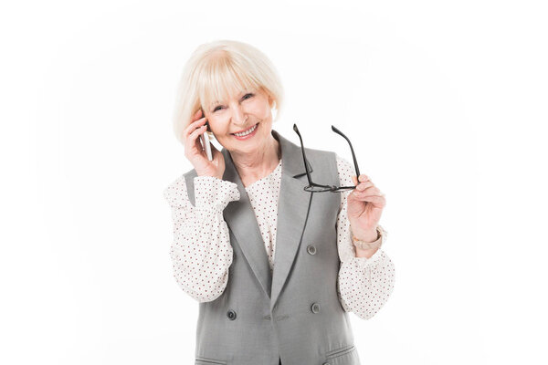 Улыбающаяся старшая деловая женщина разговаривает по смартфону и держит очки изолированными на белом

