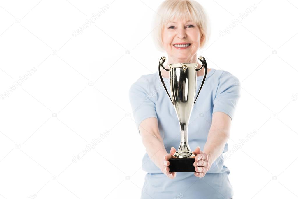 Smiling senior sportswoman holding trophy in hands isolated on white