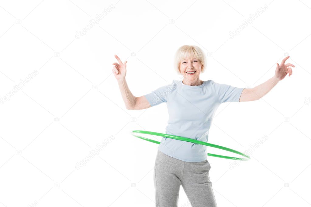 Smiling senior sportswoman doing hula hoop exercise isolated on white