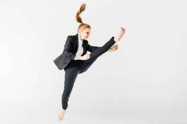 angry female karate fighter jumping and performing kick in suit isolated on grey clipart