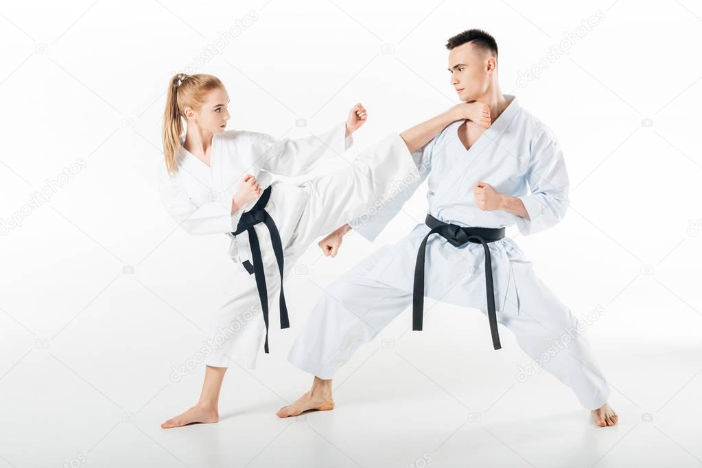 female karate fighter kicking male partner isolated on white