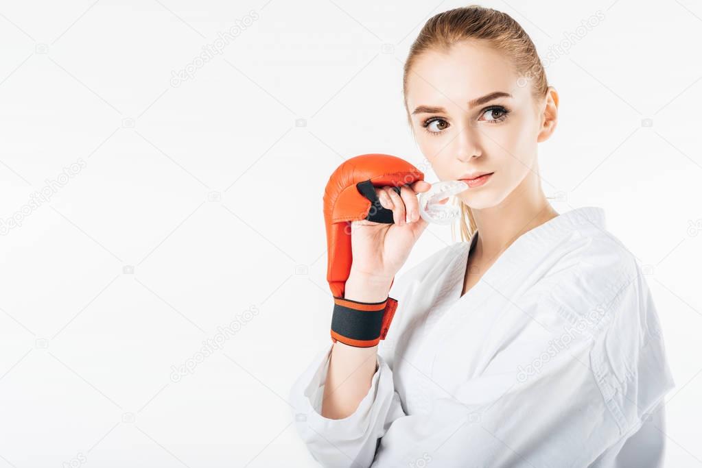female karate fighter holding mouthguard and looking away isolated on white