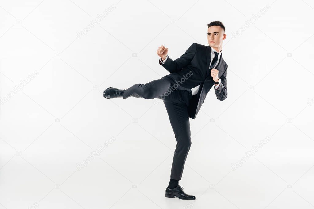 businessman in suit performing karate kick isolated on white