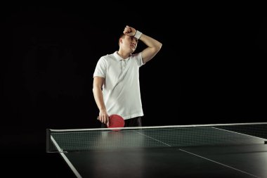 tired tennis player in uniform near tennis table isolated on black clipart