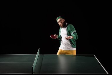 bearded sportsman with tennis equipment standing at table isolated on black clipart