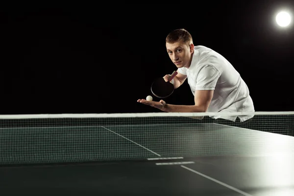 网球运动员与网球球拍和球在手站立在被隔绝的乒乓球桌在黑 — 图库照片