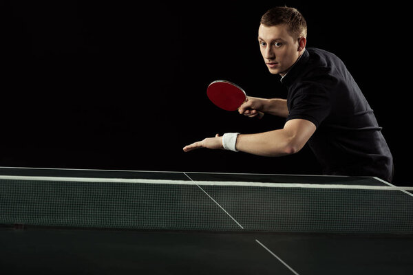 portrait of focused tennis player playing table tennis isolated on black