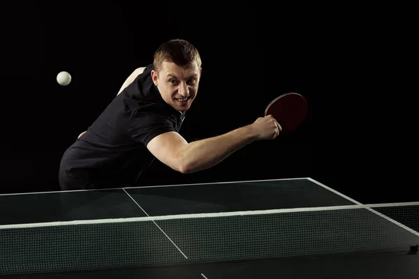 emotional tennis player in uniform playing table tennis isolated on black