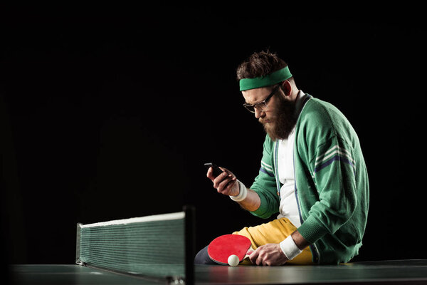 tennis player using smartphone while sitting on tennis table isolated on black